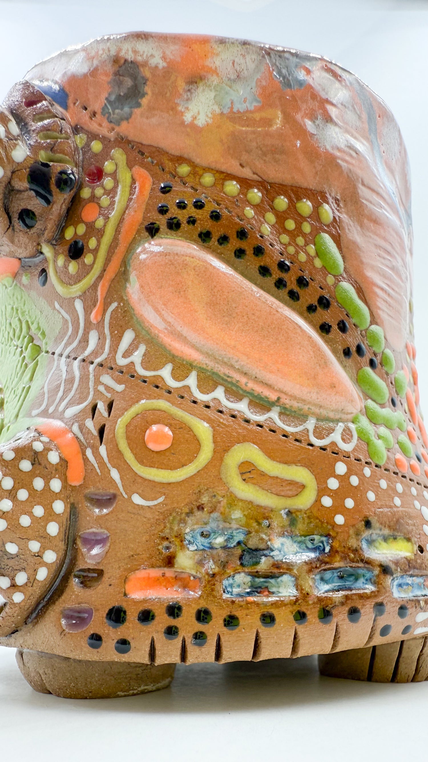 zoomed in photo of the size of a ceramic mug with lots of salmon colored  glaze, black dots, green dots, and multicolored glaze accents.
